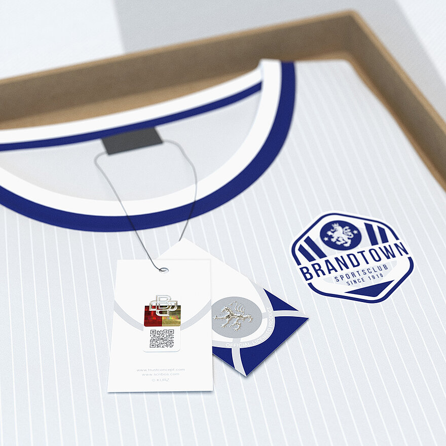 Ein mit dem Schriftzug „Brandtown Sportsclub“ versehenes Markensporttrikot in einer einfachen offenen Schachtel. Am Trikot ist ein Hangtag mit ValiGate® Trust-Technologie angebracht. Das Hangtag enthält einen QR-Code, der mit einem kopiersicheren Sicherheitsmuster und einem KURZ Trustseal-Hologramm versehen ist und einen erweiterten Fälschungsschutz sowie eine nahtlose Produktauthentifizierung bietet. Diese doppelte Sicherheitslösung bietet einen robusten Markenschutz und dient gleichzeitig als interaktiver Berührungspunkt für die Kundenbindung, der speziell auf den Lizenzmarkt zugeschnitten ist.