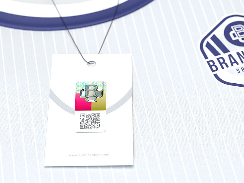 A branded sports jersey labeled “Brandtown Sportsclub” displayed inside a simple open box. Attached to the jersey is a hangtag featuring ValiGate® Trust technology. The hangtag includes a QR code embedded with a copy-proof security pattern and a KURZ Trustseal hologram, offering advanced counterfeit protection and seamless product authentication. This dual security solution provides robust brand protection while serving as an interactive touchpoint for customer engagement, tailored specifically for the licensing market.