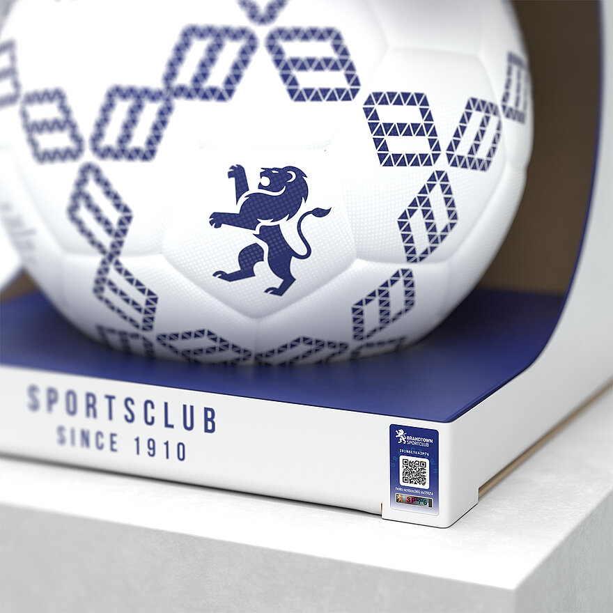 一个印有蓝色几何图案和狮子徽章的白色足球，包装上印有“Sportsclub Since 1910”字样。足球采用激光光刻VeoMark®技术，集公开和隐蔽防伪功能于一体，可有效防止假冒。该解决方案可确保产品真实性，提升品牌信任度。