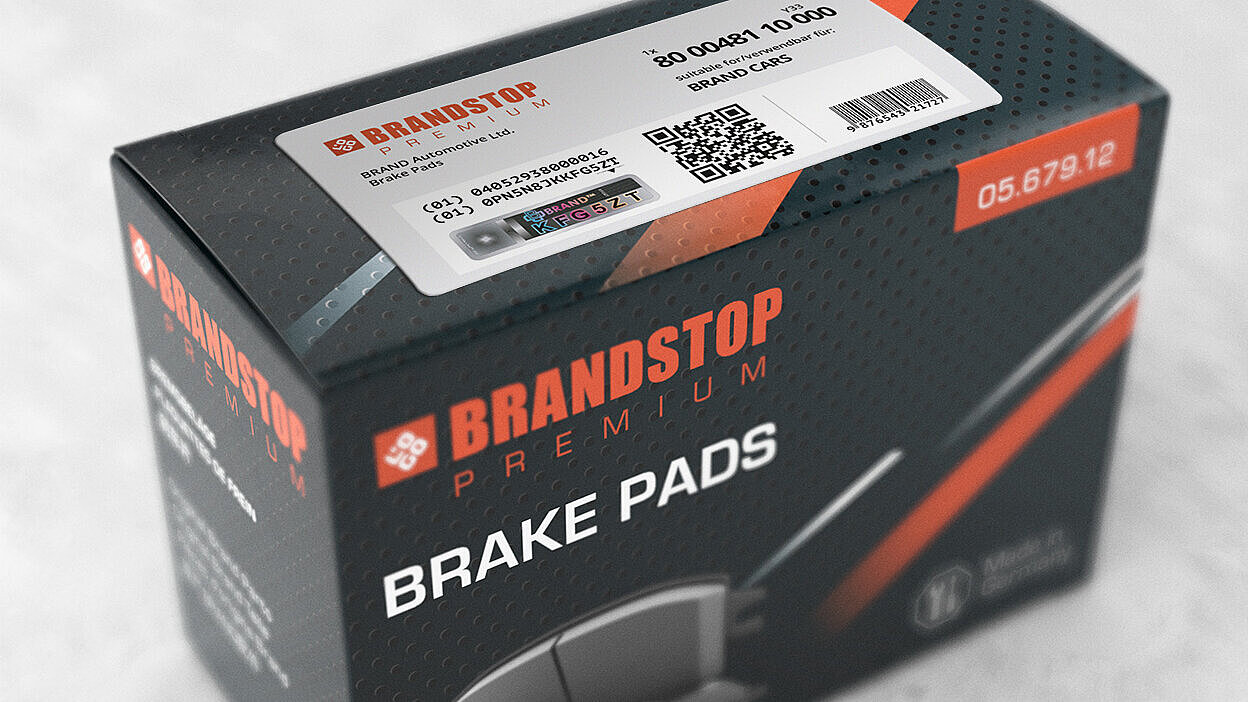 A rectangular box of Brandstop Premium Brake Pads with a security label affixed to its surface. The label features a QR code, product information, and a distinctive security element with a holographic design displaying colorful alphanumeric characters (KFG5ZT) under the VeoMark® branding. The label showcases advanced counterfeit protection technology with a mix of overt and covert security features.